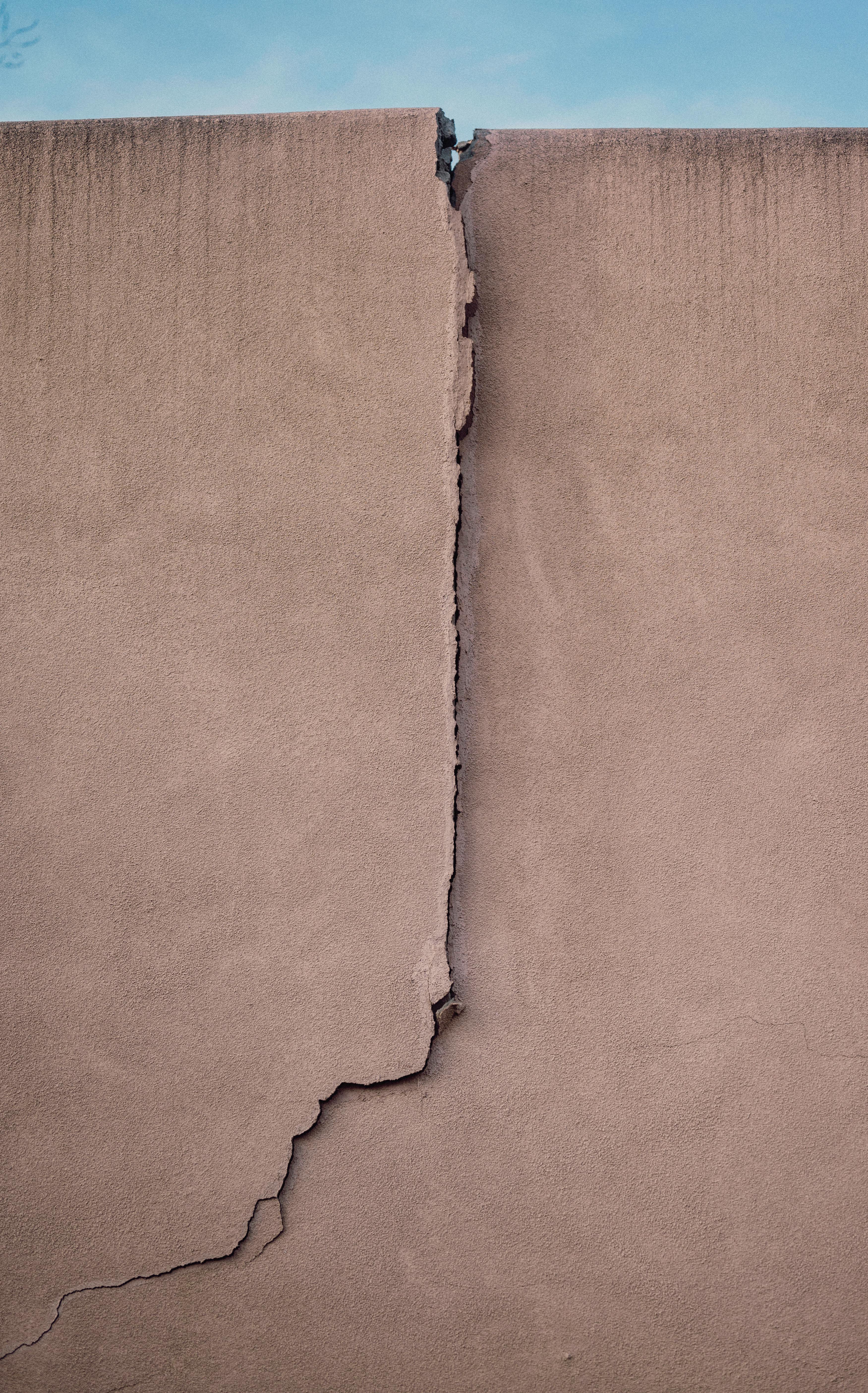 A close-up of a vertical cracked concrete wall against a clear sky.