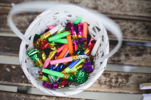 Top view of a white wicker basket filled with colorful party blowouts on wooden surface.