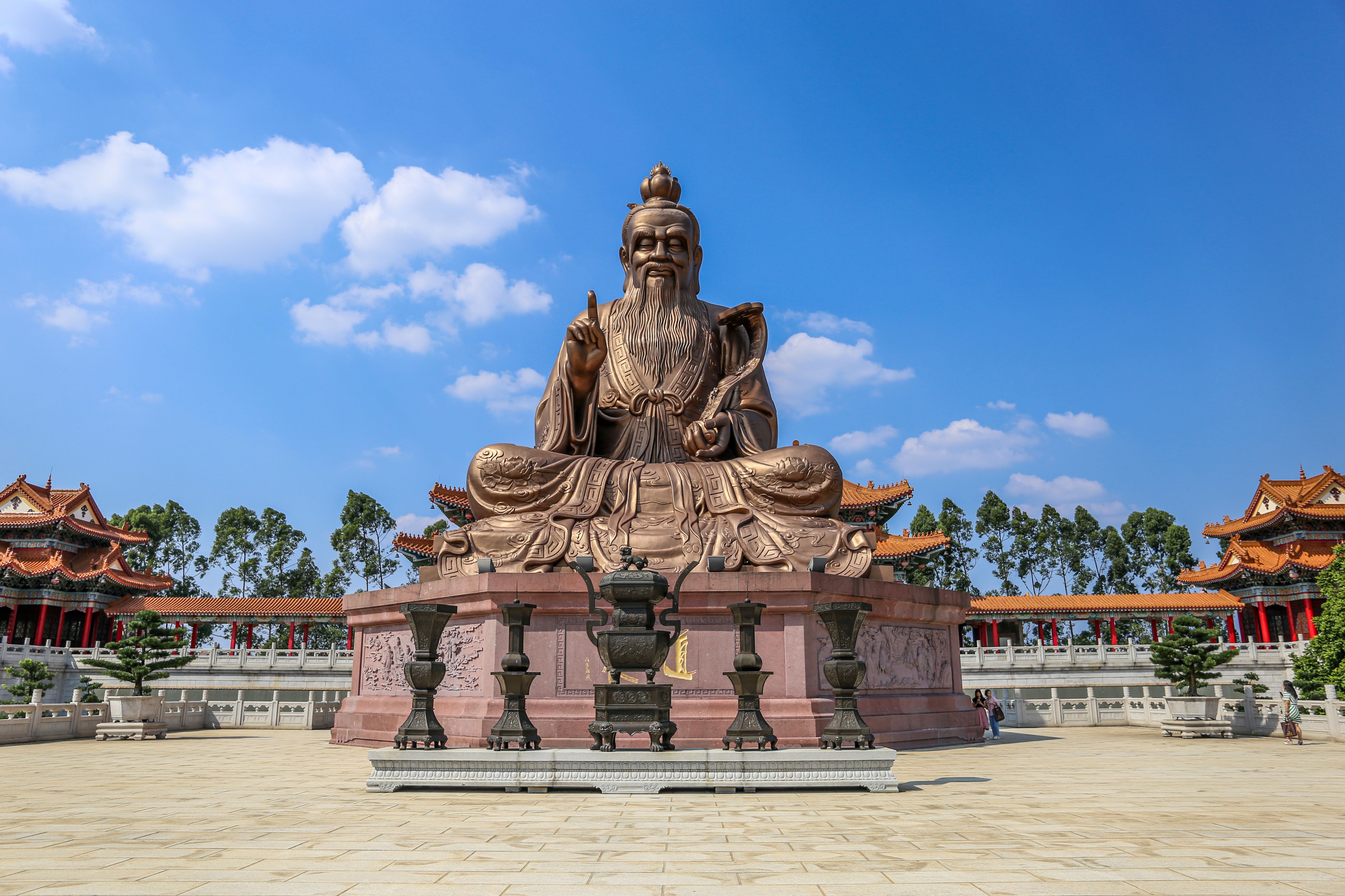 Majestic statue of Laozi in a sunlit temple courtyard under a blue sky.