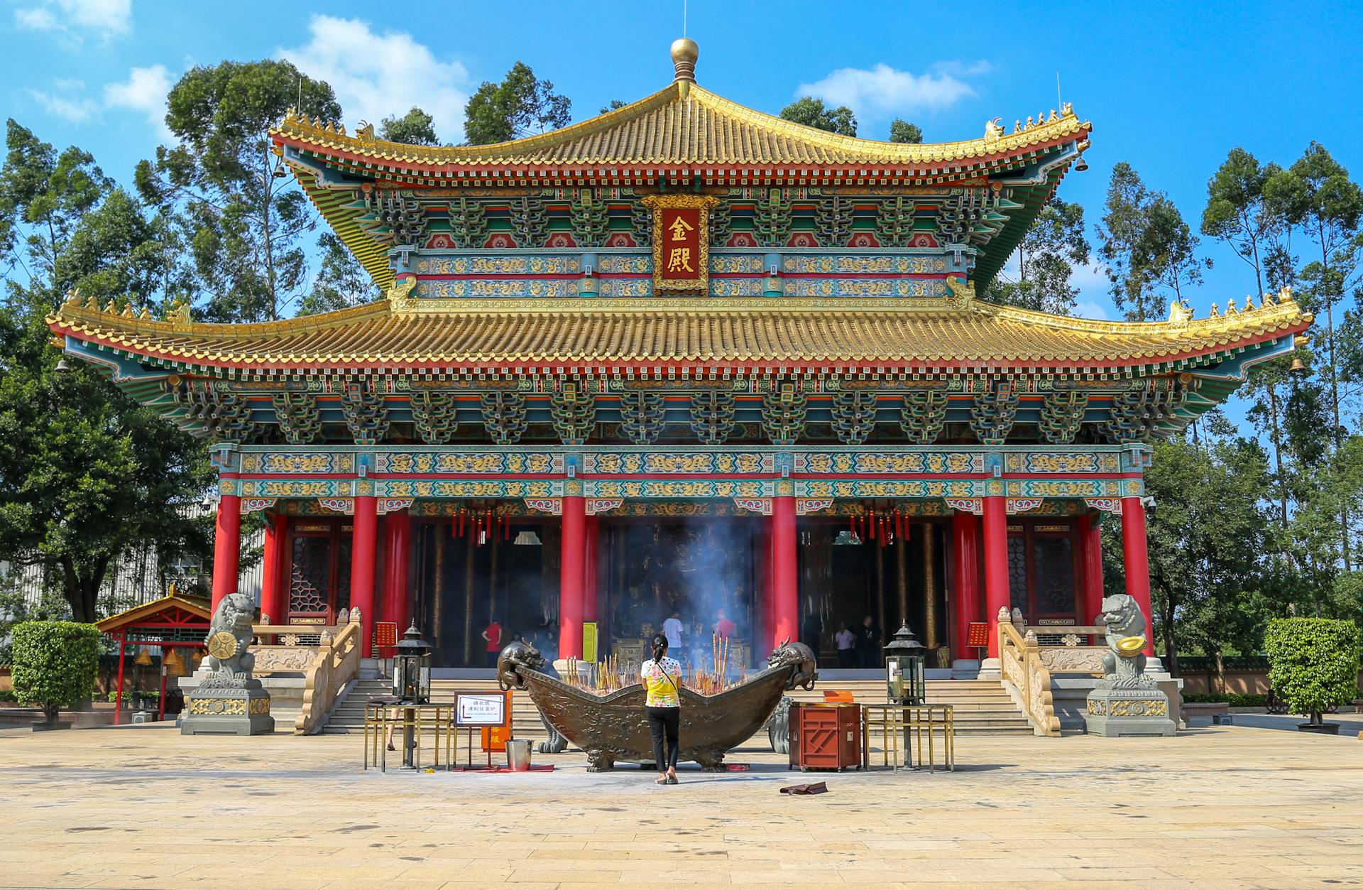 A vibrant traditional Chinese temple with intricate architectural details and an incense burner in front.