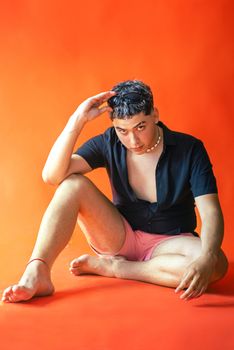 A fashionable young man in shorts and sunglasses poses confidently against an orange backdrop.
