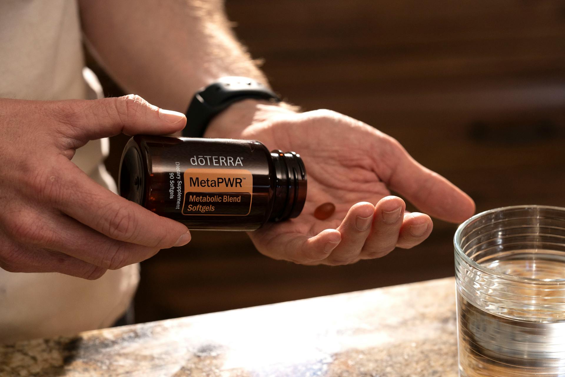 Hand holding MetaPWR metabolic blend softgels next to a glass of water.