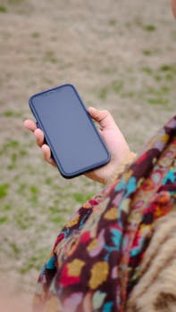 Close-up of a smartphone in hand with colorful scarf in an outdoor setting. Ideal for technology and lifestyle themes.