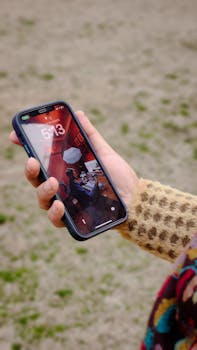 A hand holding a smartphone with a vivid home screen outdoors in a grassy area.