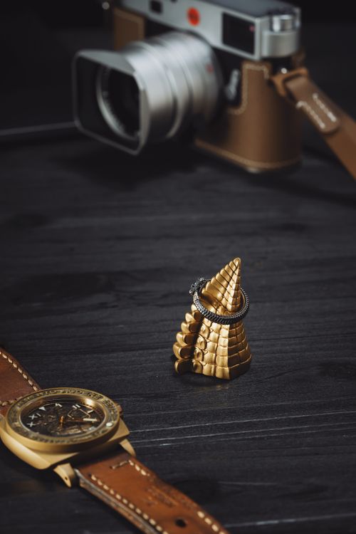 Free Elegant golden ring holder on a dark table with camera and leather watch, showcasing style and luxury. Stock Photo