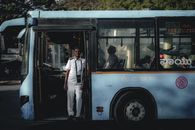 Bus driver wearing a white uniform standing by the bus door, sunlight casting shadows inside