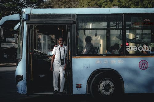 Free Bus driver wearing a white uniform standing by the bus door, sunlight casting shadows inside Stock Photo