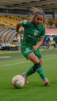 A female football player skillfully dribbling during a match in a soccer stadium.