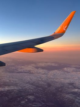 A stunning view of an airplane wing over Adana, Türkiye, with a scenic landscape at sunset.