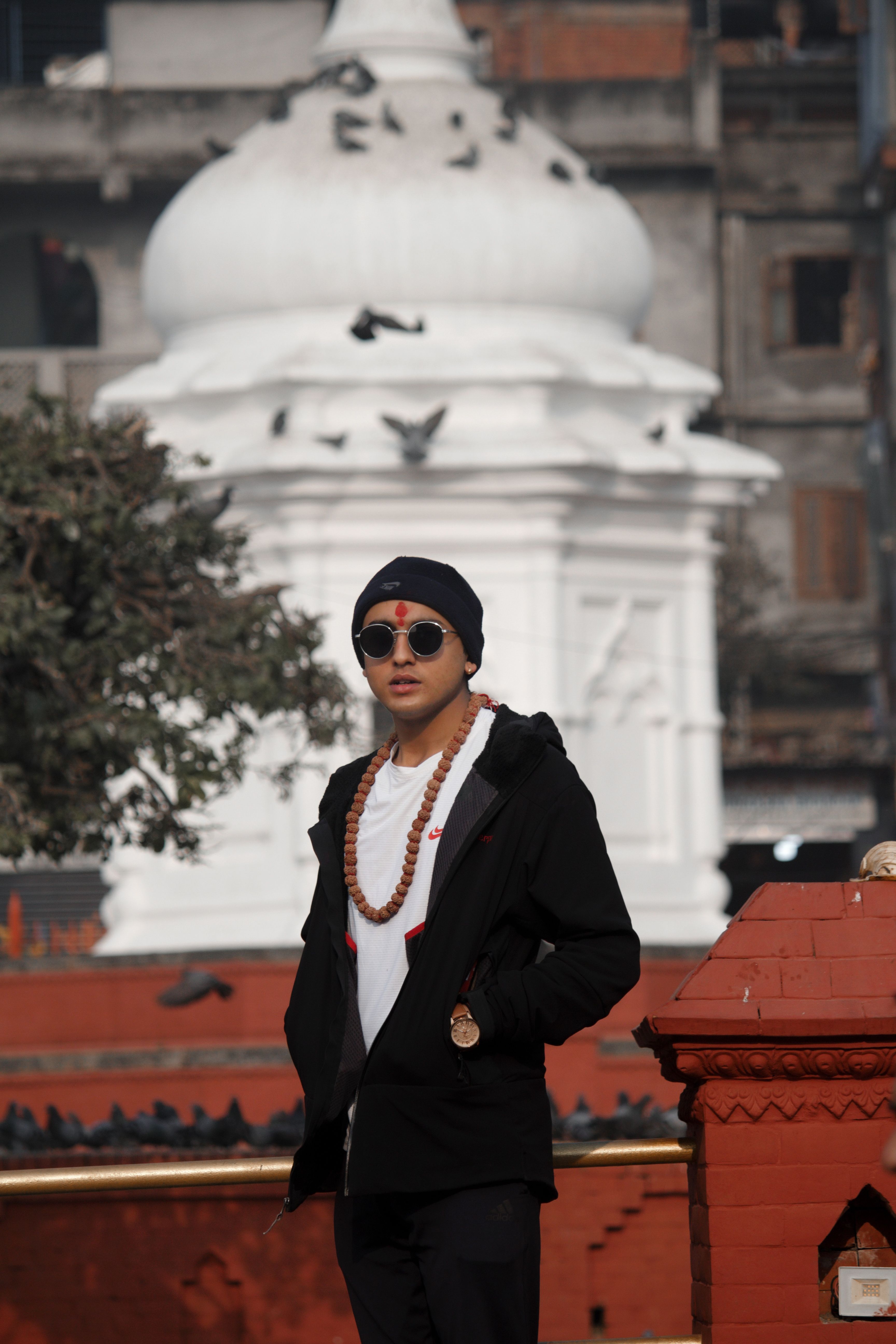 Person in fashionable attire with sunglasses standing before a historic monument, conveying urban style.