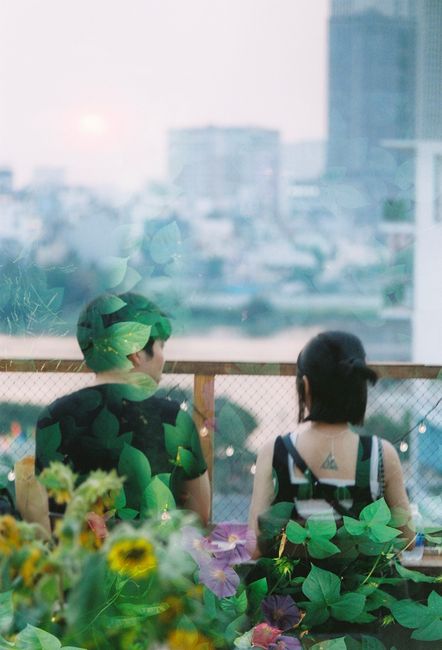A couple enjoys a serene moment on a leafy rooftop balcony overlooking the city at twilight.