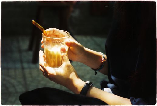 Close-up of hands holding iced coffee in a glass with a straw, soft focus and warm tones.