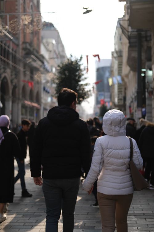 Free A couple walks hand in hand on a busy street in an urban setting, surrounded by pedestrians. Stock Photo
