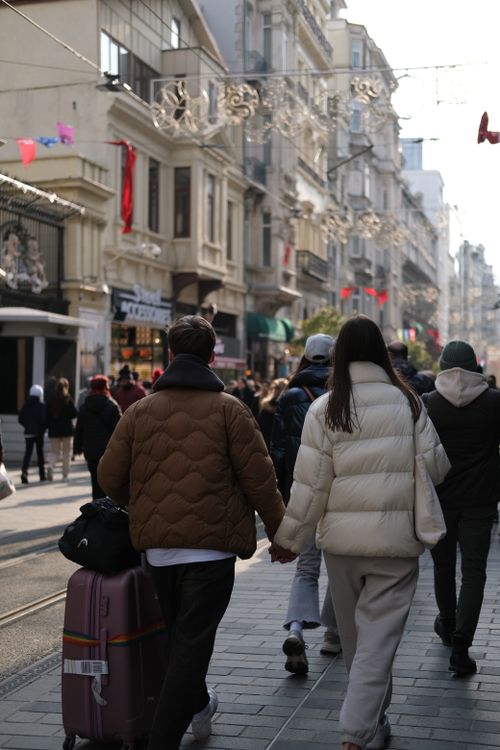 Free A couple holding hands and walking through a lively urban street filled with people and shops. Stock Photo