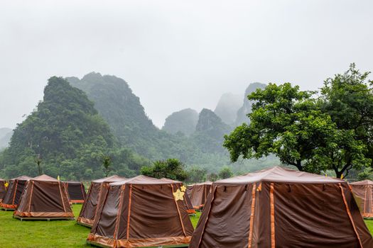 Tents in a lush green campsite with scenic mountains in the background on a misty summer day.