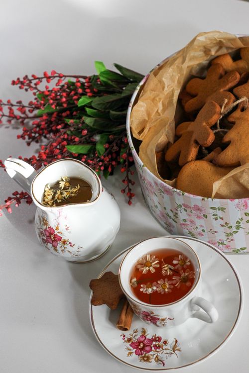 Free Charming tea setup with floral teacups, herbal tea, and gingerbread cookies in a decorative tin. Stock Photo