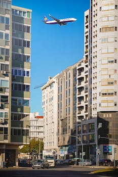 A city street in Lisbon with a plane flying overhead against a clear sky.