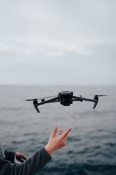 A close-up shot of a drone hovering over the ocean with a human hand interacting.