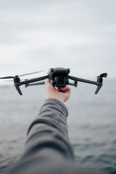 A person holding a drone over a vast ocean horizon, ready to launch into the sky.