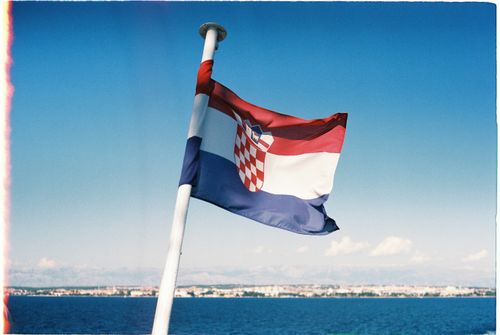 Free Croatian flag waving on a flagpole with a clear blue sky and sea view in Zadar. Stock Photo