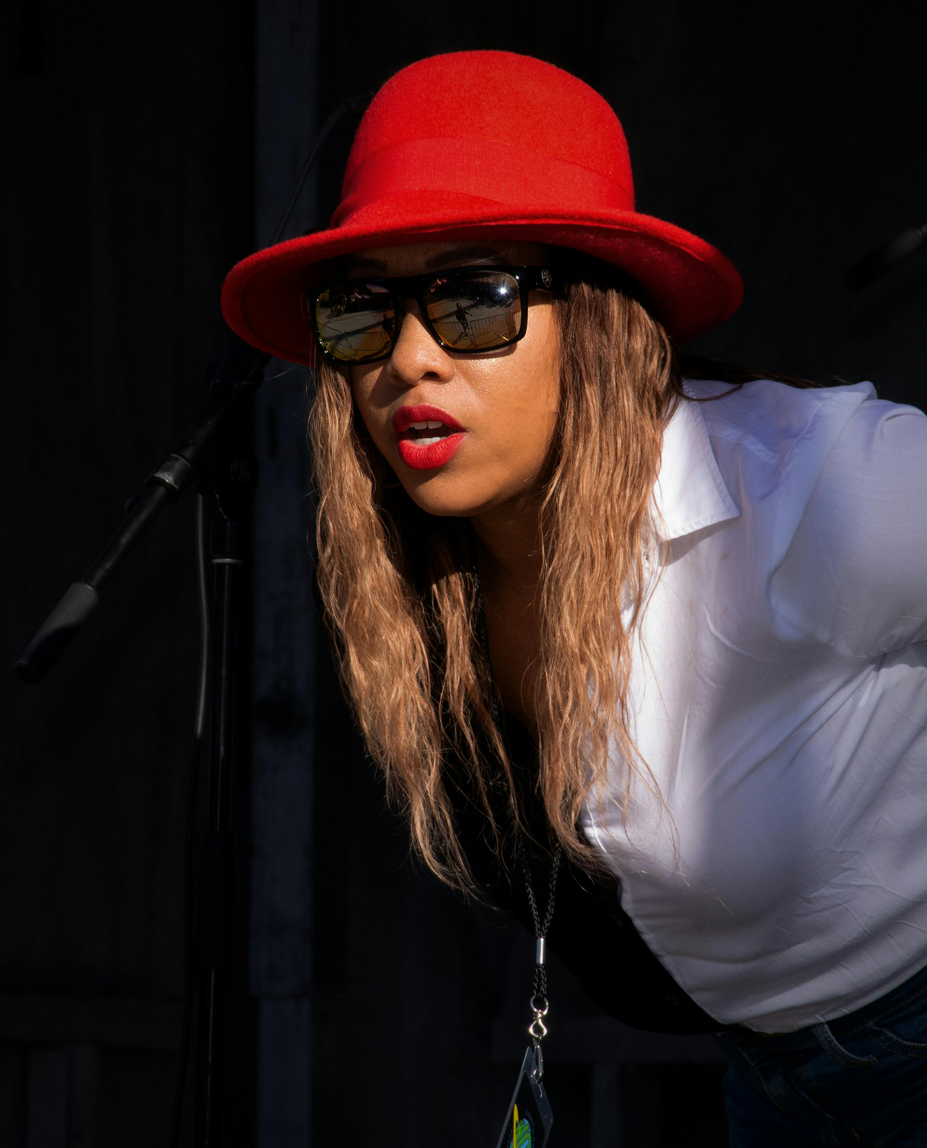 A fashionable woman wearing a red hat and sunglasses performs on stage in Tulsa, OK.