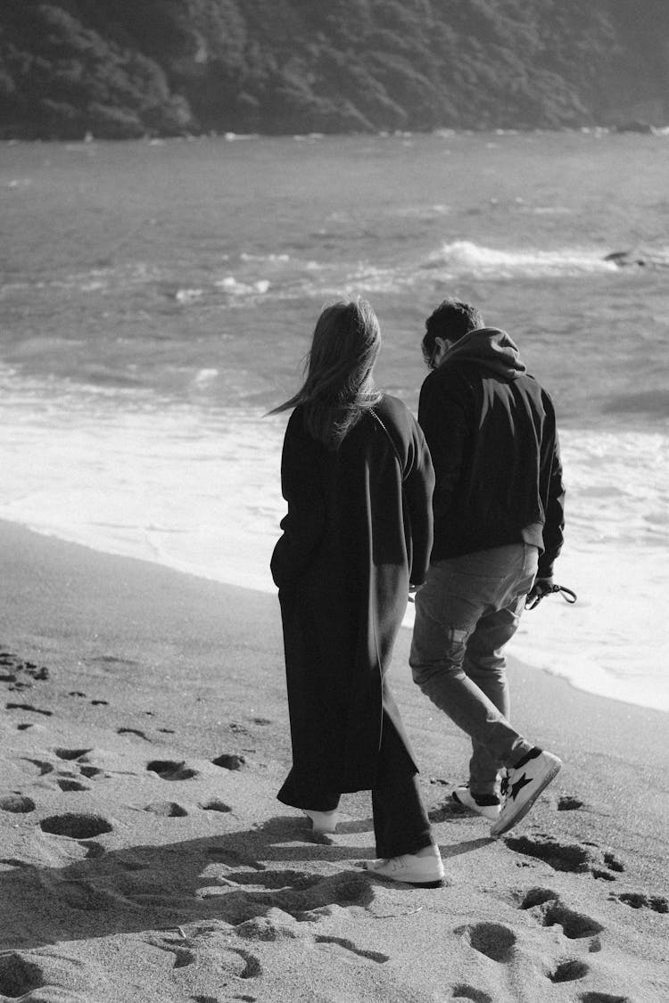 Black And White Photo Of A Young Couple Walking On The Beach