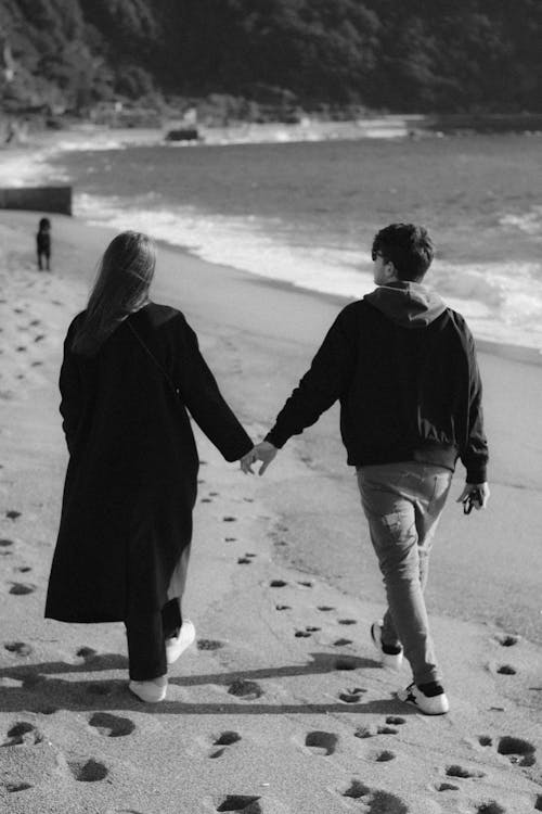 Black and White Photo of a Young Couple Walking on the Beach Holding Hands
