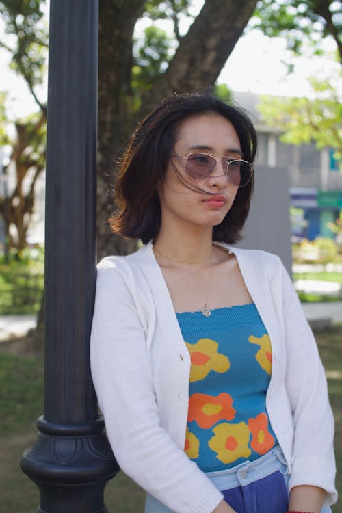 A woman wearing sunglasses and a floral top is standing next to a lamp post
