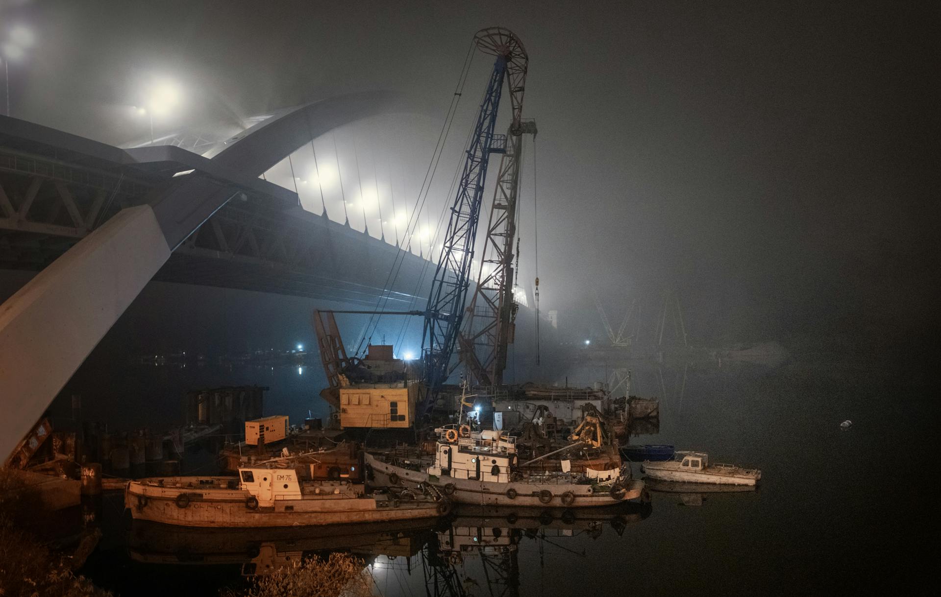 Misty night at a shipyard with a towering crane and illuminated bridge.