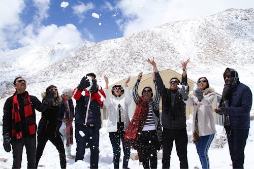 Group of People Standing in a Mountain Valley, Throwing Snow in the Air and Smiling 