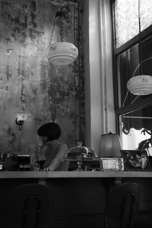 Black and White Photo of Woman Sitting behind Bar Counter