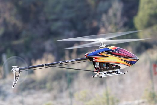 Colorful remote control helicopter flying outdoors, showcasing dynamic motion against blurred natural backdrop.