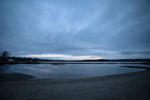Captivating overcast shoreline of Stamford, CT at dusk with tranquil waters and distant town view.
