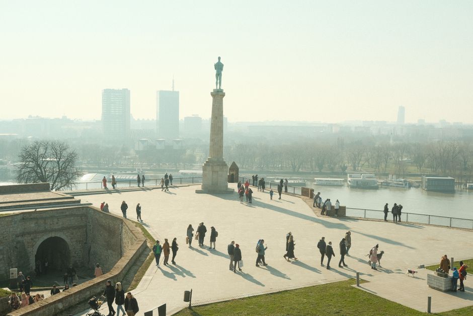 Scenic view from Belgrade Fortress overlooking the city and river, people walking in the plaza.