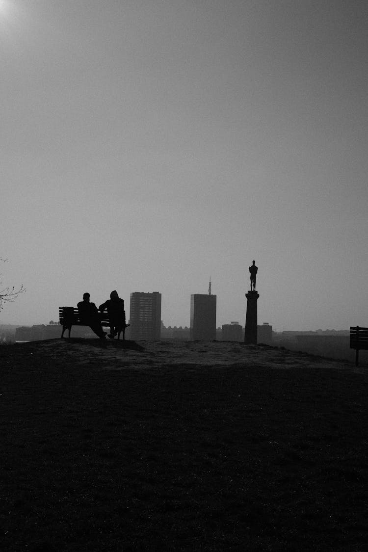 Silhouettes Of People Sitting On Bench On Hill Overlooking City