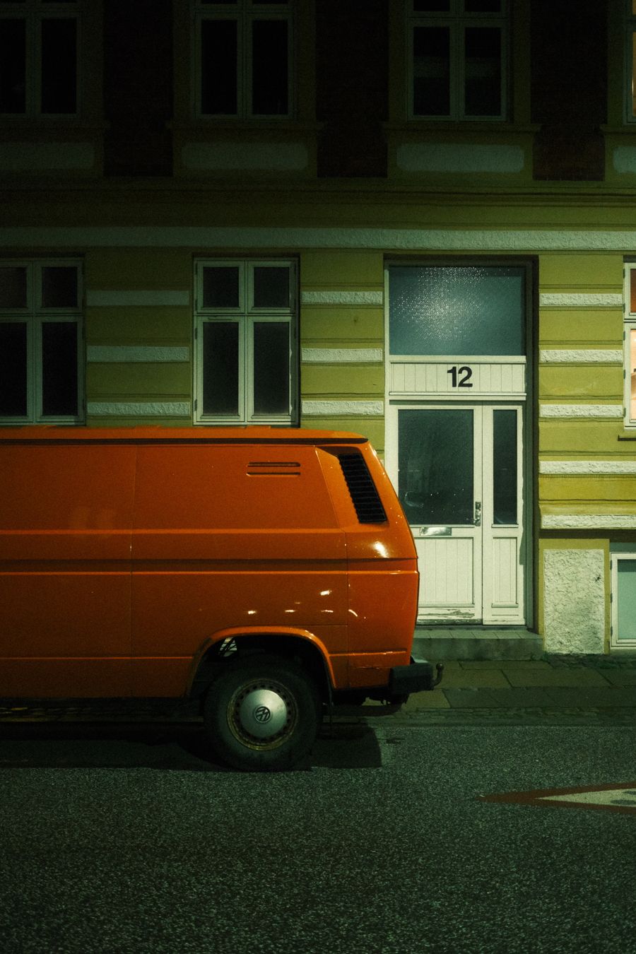 A trade van parked outside a house on a dark street at night, the doorway lit above the step