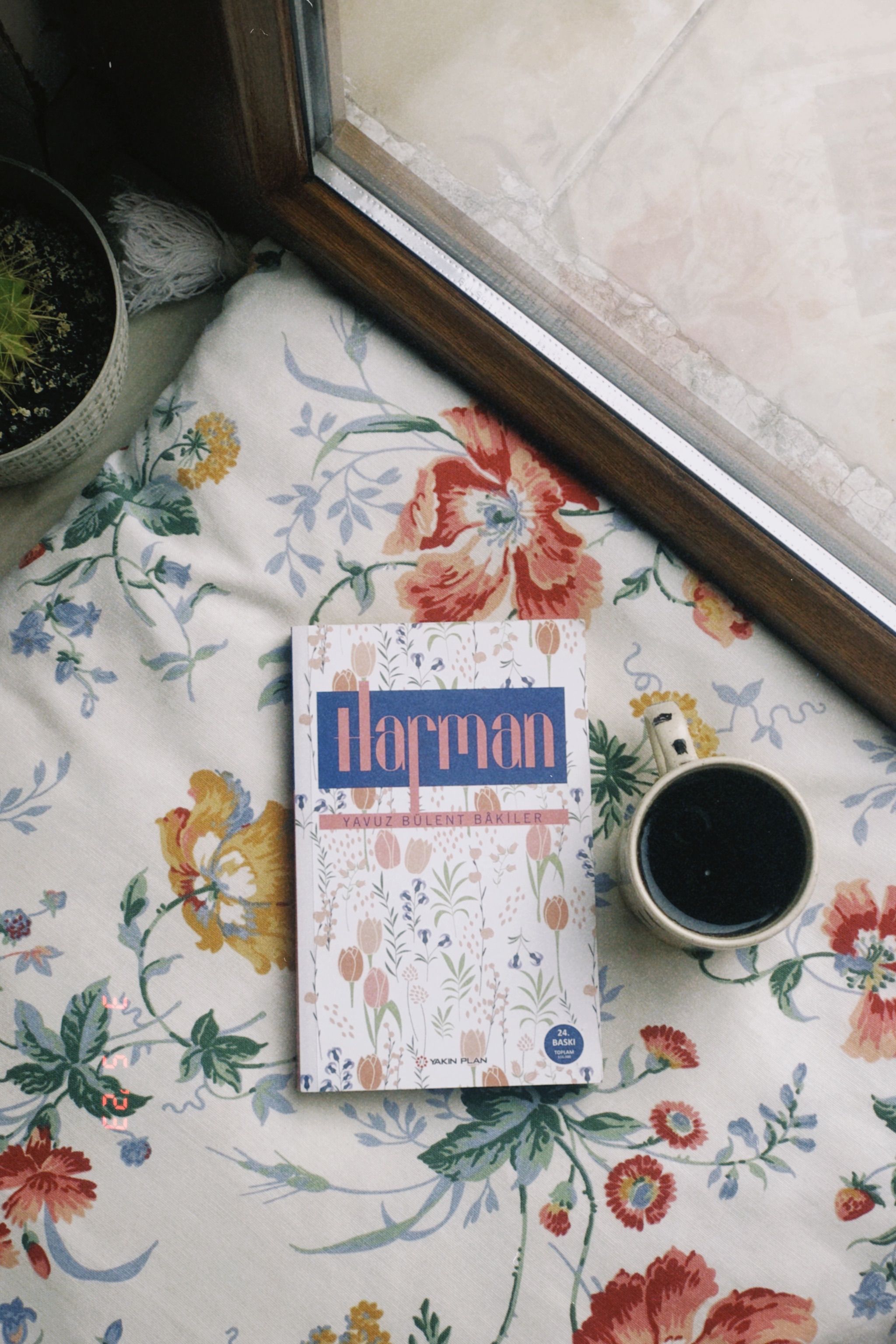 A still life of a book and coffee mug on floral fabric, creating a cozy indoor vibe.