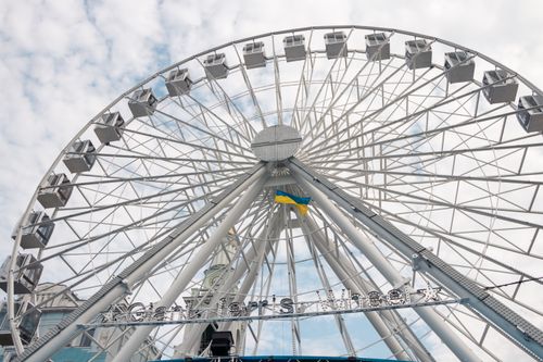 Free A striking view of a ferris wheel with a Ukrainian flag on a cloudy day. Stock Photo