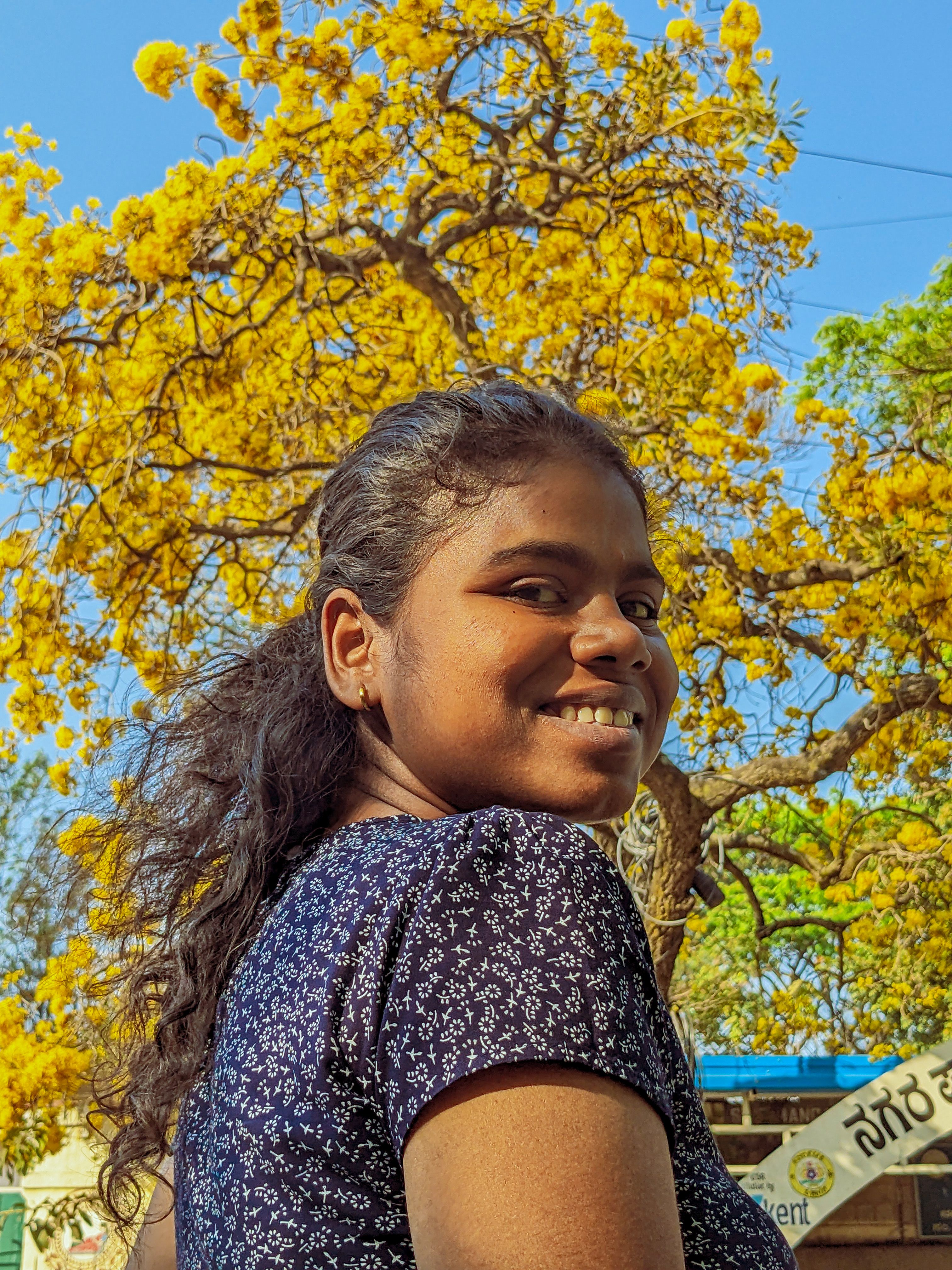 Happy woman with curly hair smiling under a bright yellow tree in an outdoor autumn setting.