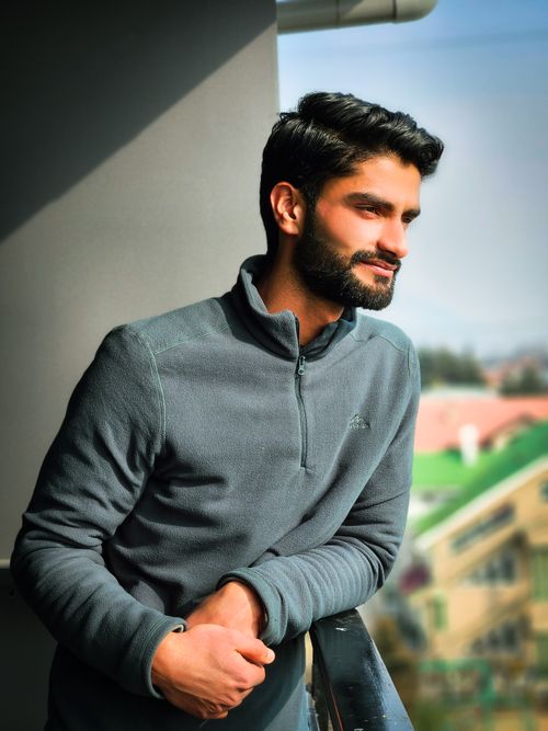 Free A relaxed man in a gray sweater enjoys a sunny day outdoors, leaning on a railing. Stock Photo