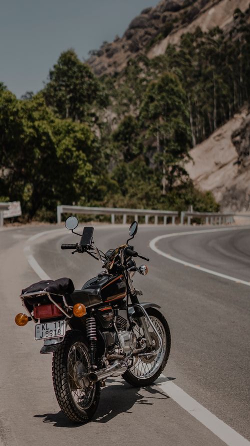 Free A classic motorcycle parked on a winding mountain road surrounded by lush green forest. Stock Photo