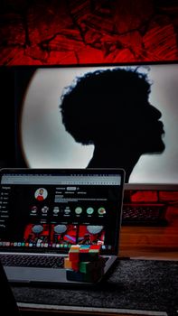 Silhouette of person behind laptop with Rubik's cube on desk, modern studio setup.