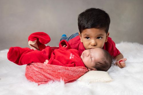 Free Cute siblings bonding with a baby and toddler on a soft white bed indoors. Stock Photo