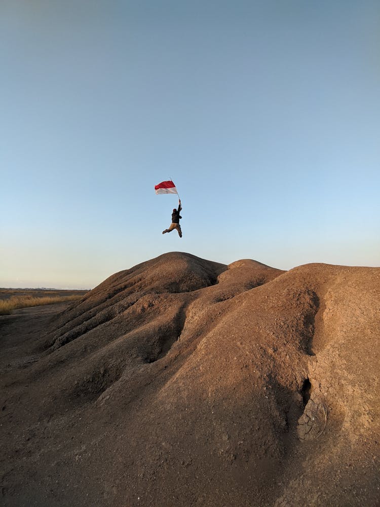 Person With Flag Of Indonesia Jumping On Barren Rocks