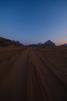 A captivating desert scene with prominent tire tracks leading to distant mountains under a twilight sky.