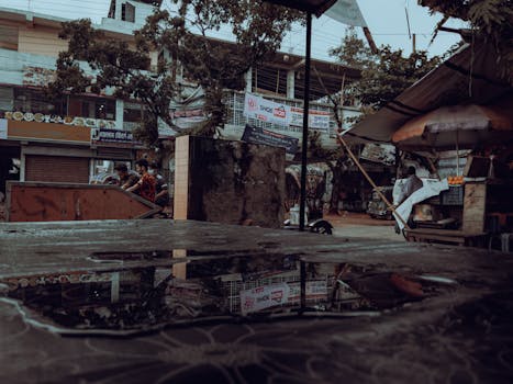 Moody urban street scene with puddles reflecting buildings and activity after rain.