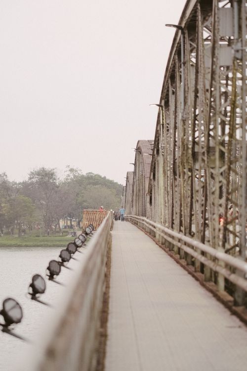 Free A moody scene of a pedestrian bridge over a river on an overcast day, featuring architectural details. Stock Photo