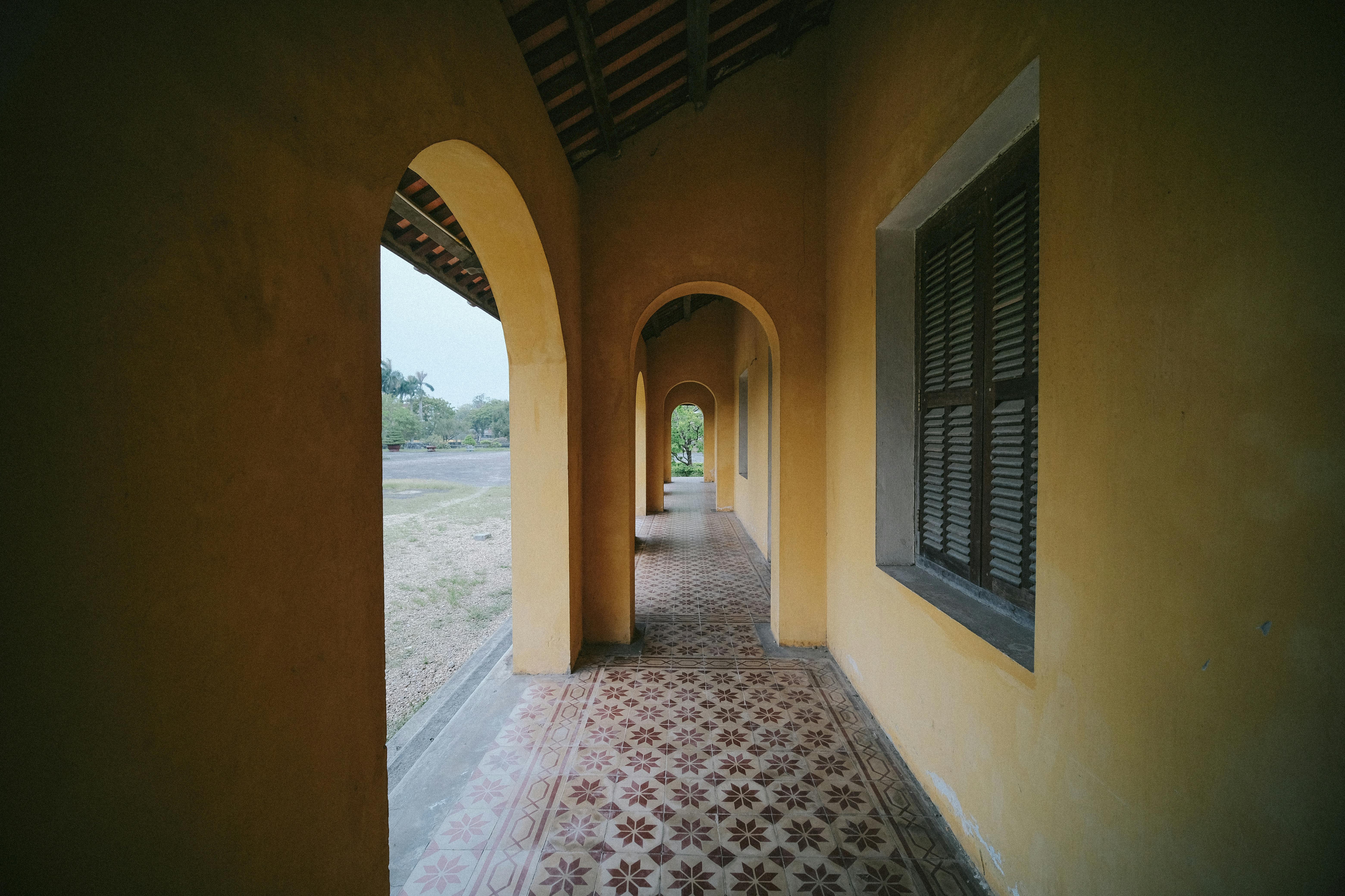 Charming corridor with yellow walls, arches, and detailed tiled floor in Vietnam's historic architecture.