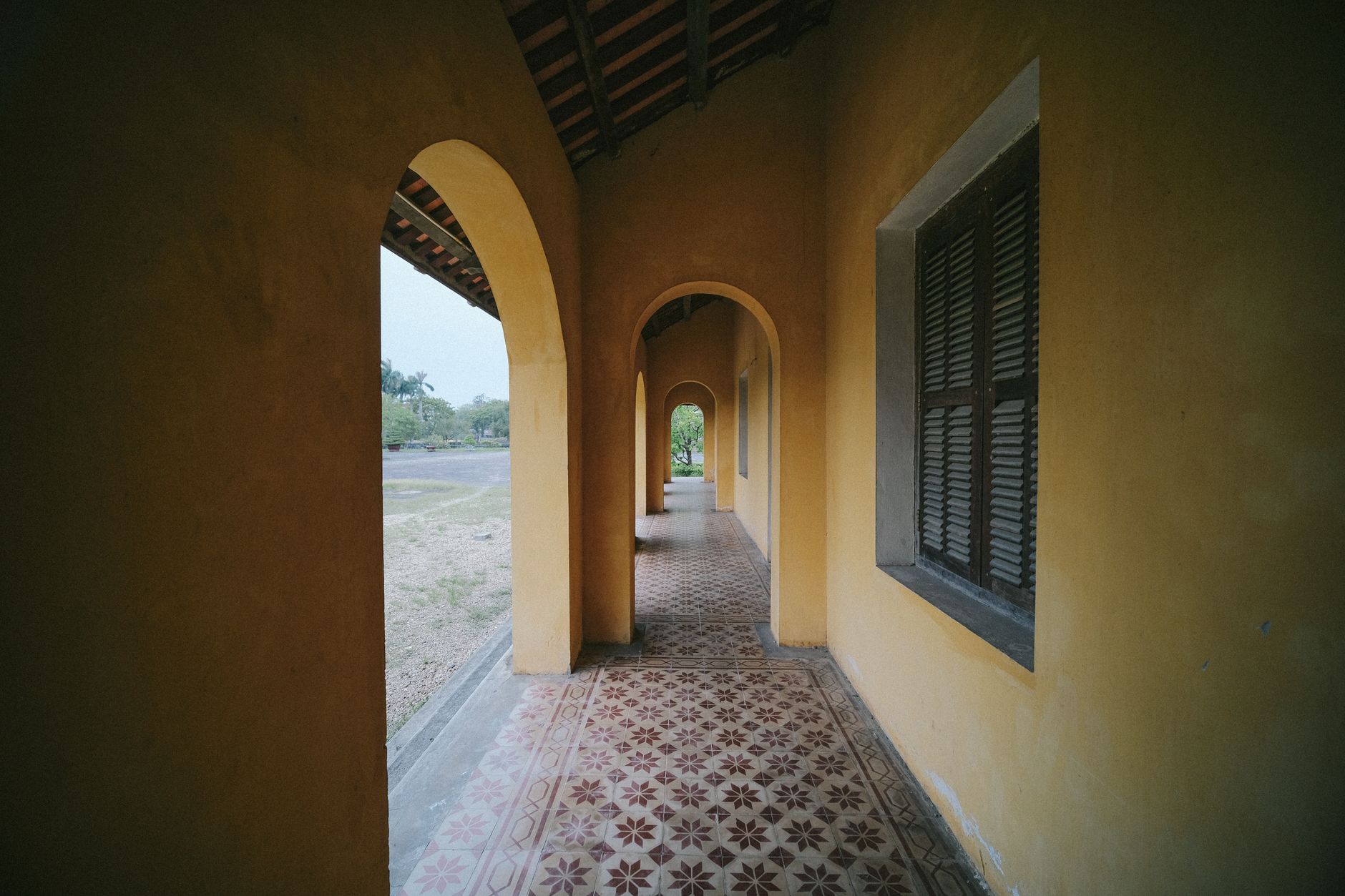 Charming corridor with yellow walls, arches, and detailed tiled floor in Vietnam's historic architecture.
