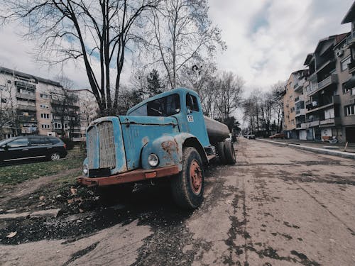 A Broken Rusty Truck Parked on the Side of the Street in City 